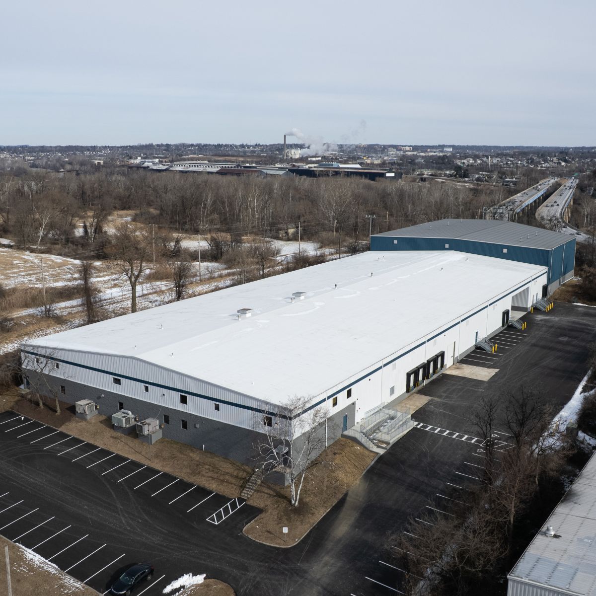 Aerial view of an industrial property featuring a large building and surrounding parking area.