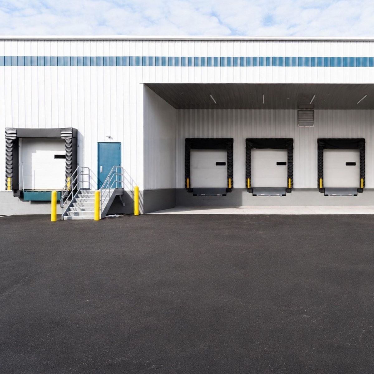 Exterior view of a commercial building with multiple loading dock entrances and an adjacent door with stairs.